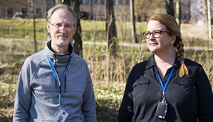 Older man and younger woman standing outside, smiling.